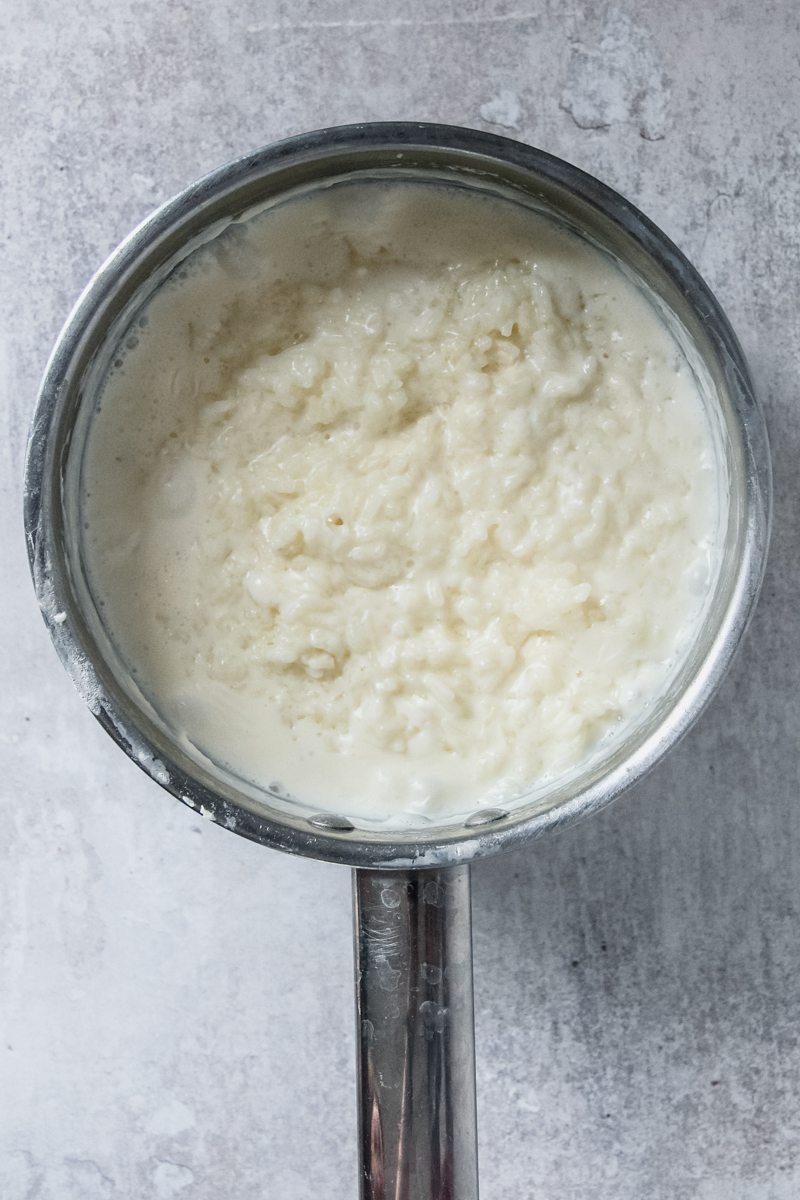 Rice pudding sits in a stainless steel saucepan on a gray surface.