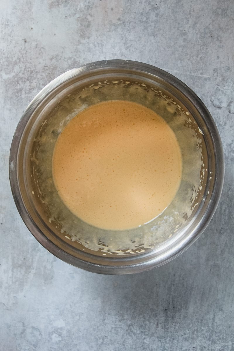 Whipped egg yolks and sugar sit in a stainless steel bowl on a gray surface.