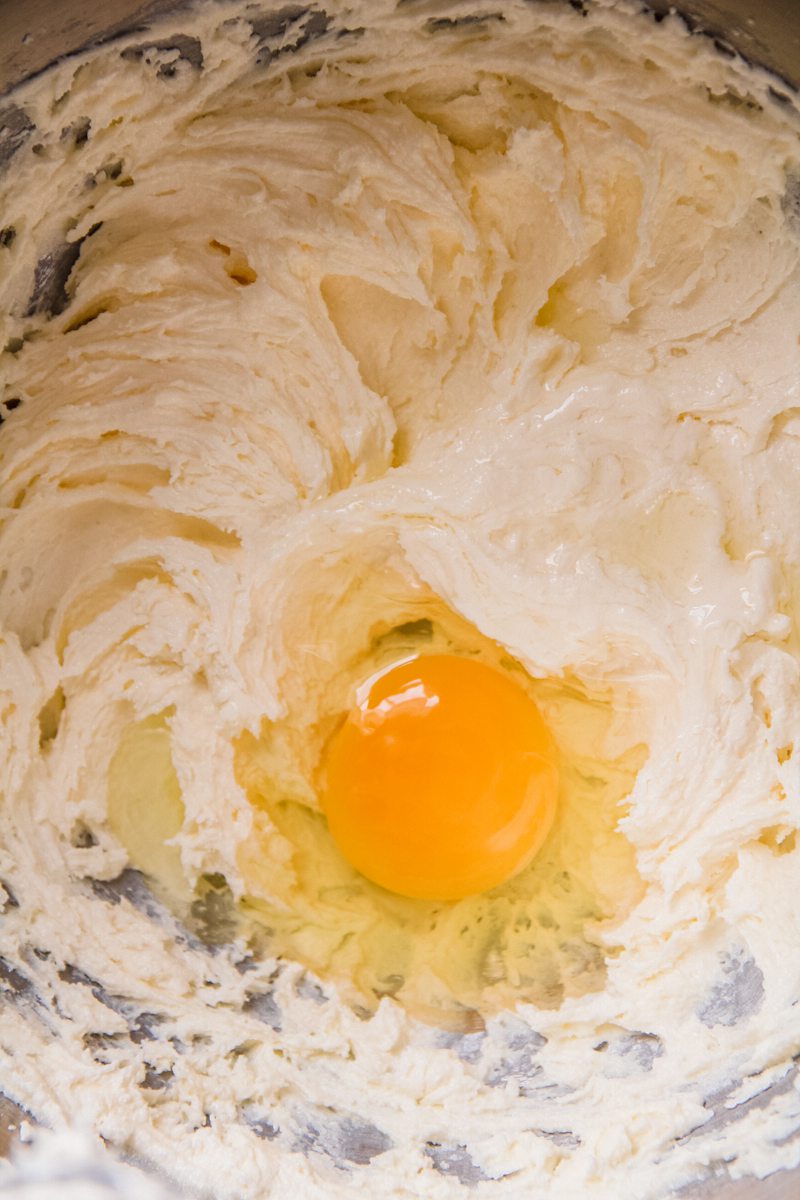 A egg sits on top of a whipped butter and sugar mixture in a stainless steel bowl.