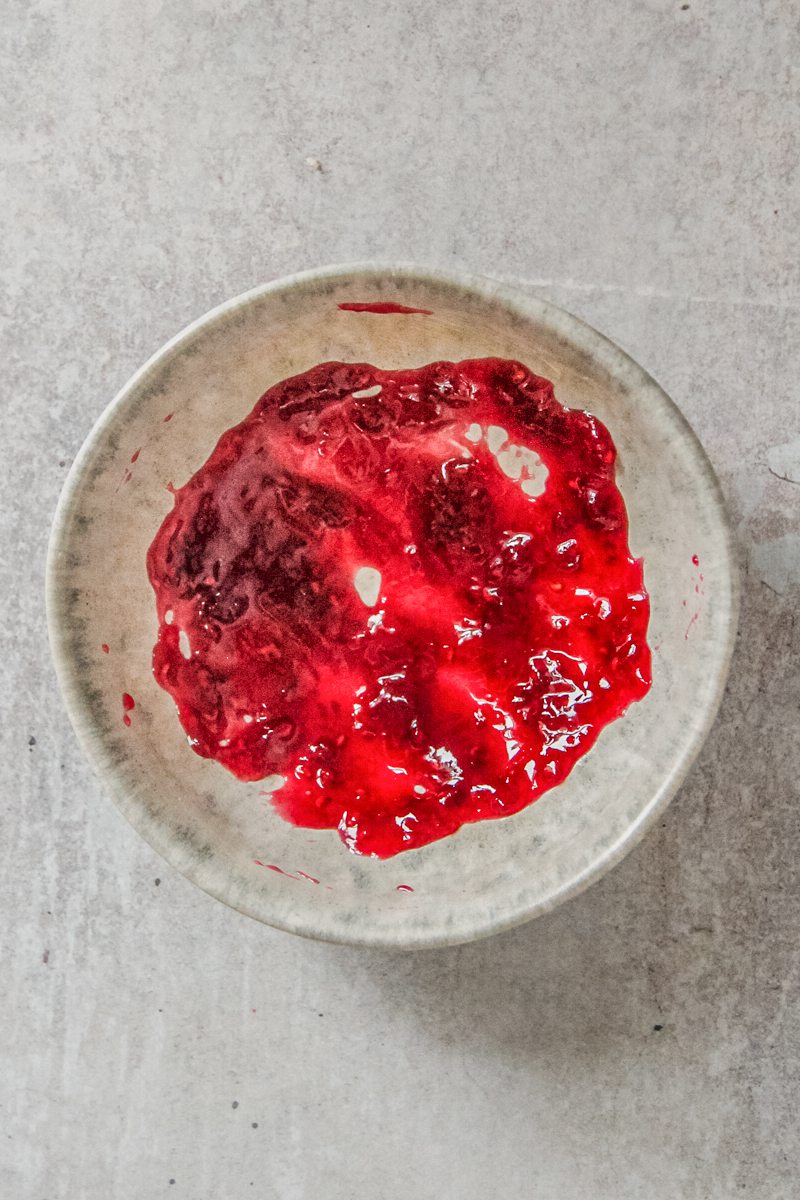 Jam sits spread over the base of a blue ceramic bowl on a gray surface.
