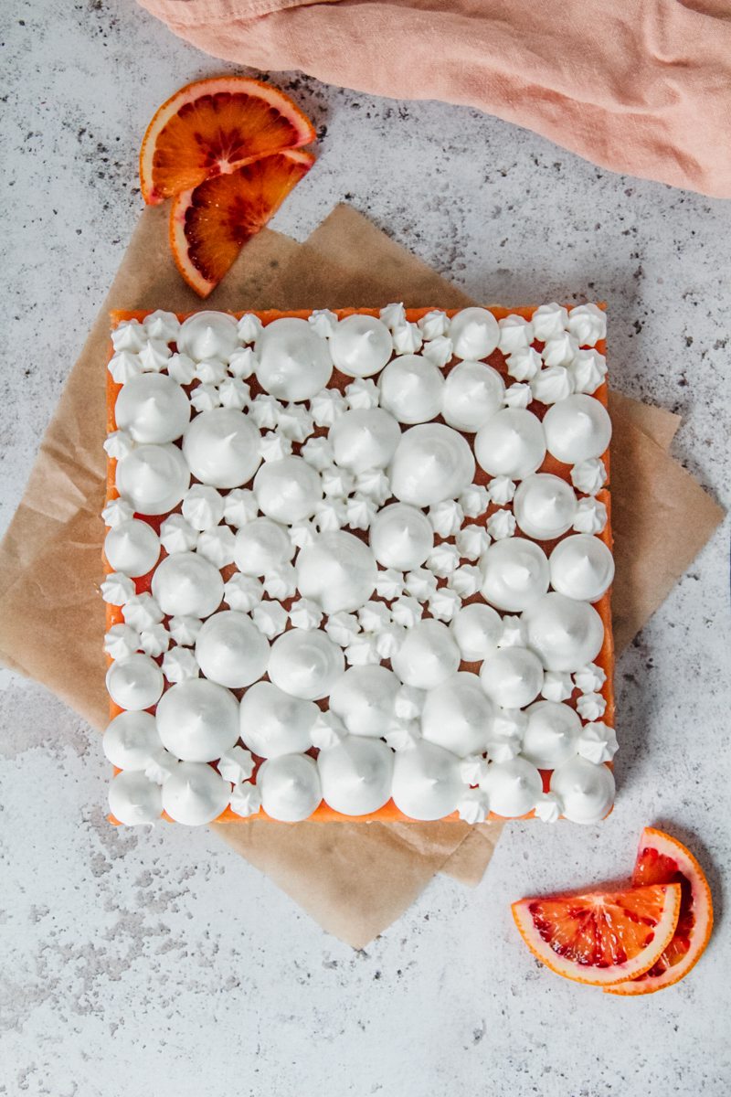 Piped Swiss meringue sits on top of blood orange curd bars on a light gray surface.