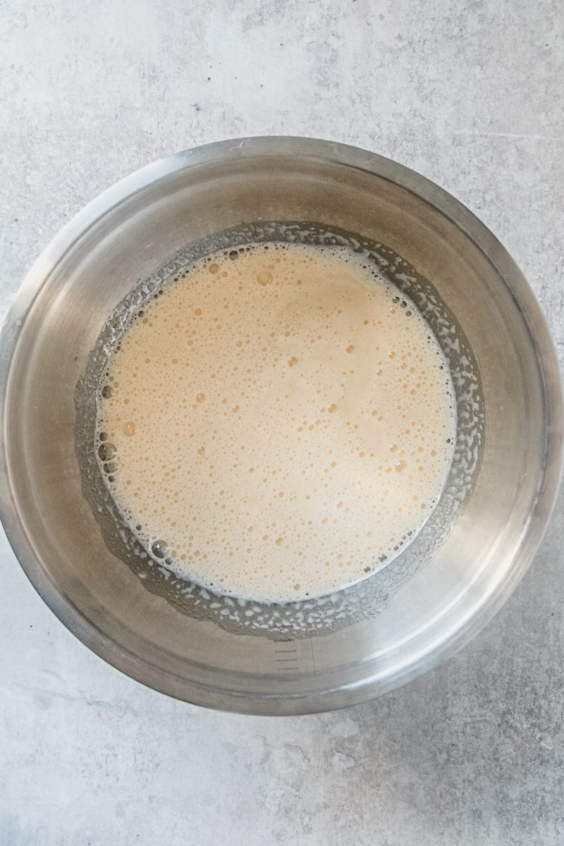 Whipped eggs and sugar sit in a stainless steel bowl on a gray surface.