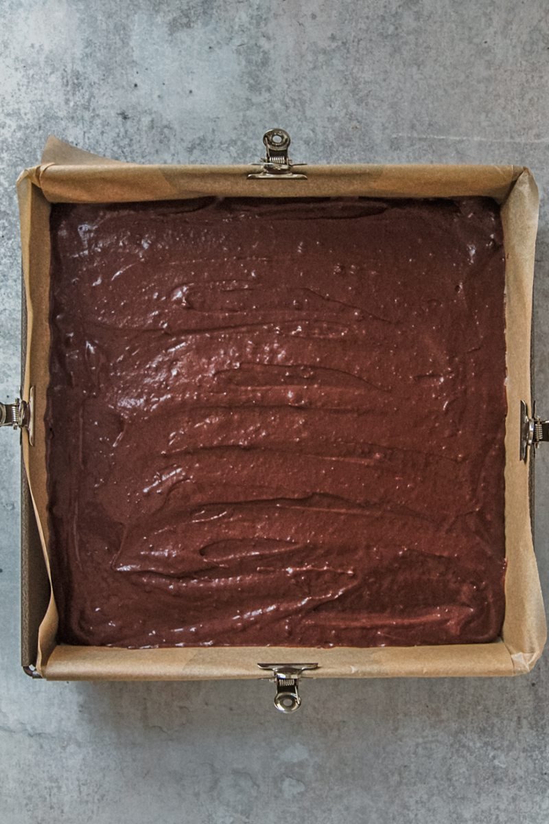 Swedish Love Cake batter sits in a lined square metal cake tin on a gray surface.