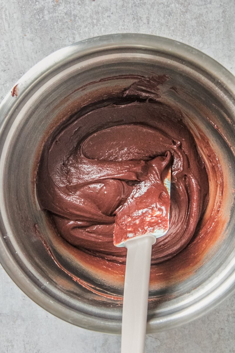 Chocolate frosting sits in a stainless steel bowl on a gray surface.