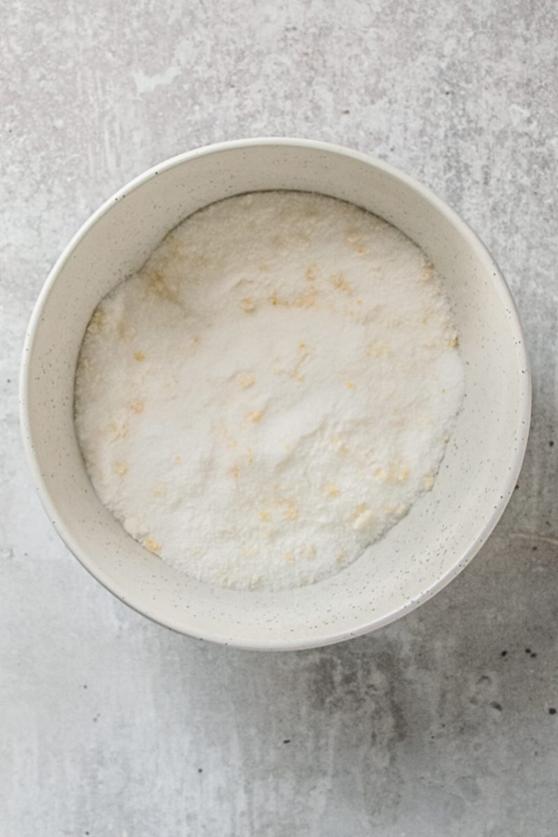 Sugar and finely chopped lemon peel sit in a gray ceramic bowl on a gray surface.