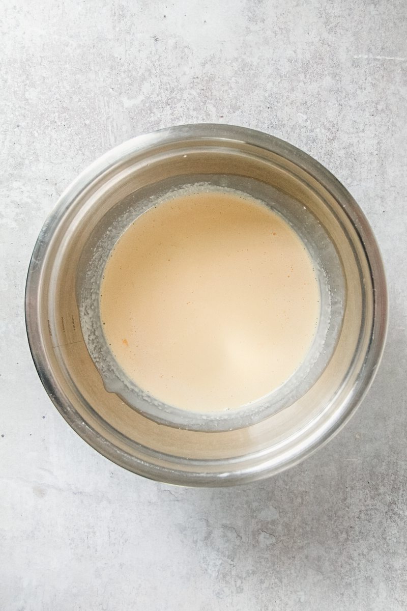 A whipped egg mixture sits in a stainless steel bowl on a gray surface.