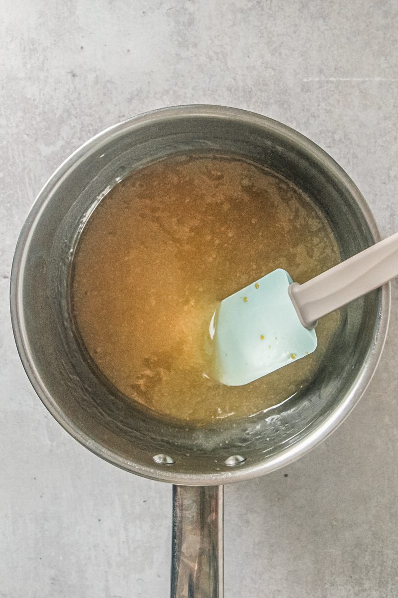 A cooked lemon juice mixture sits in a stainless steel saucepan on a gray surface.