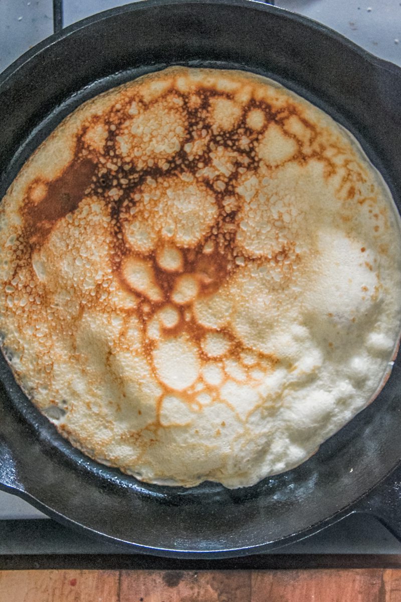 A pancake sits in a cast iron skillet on a cooker.