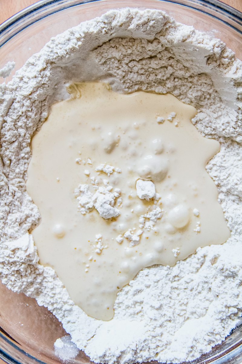 Cream and lemonade sit in the well of a dry mixture in a glass bowl on a wooden background.