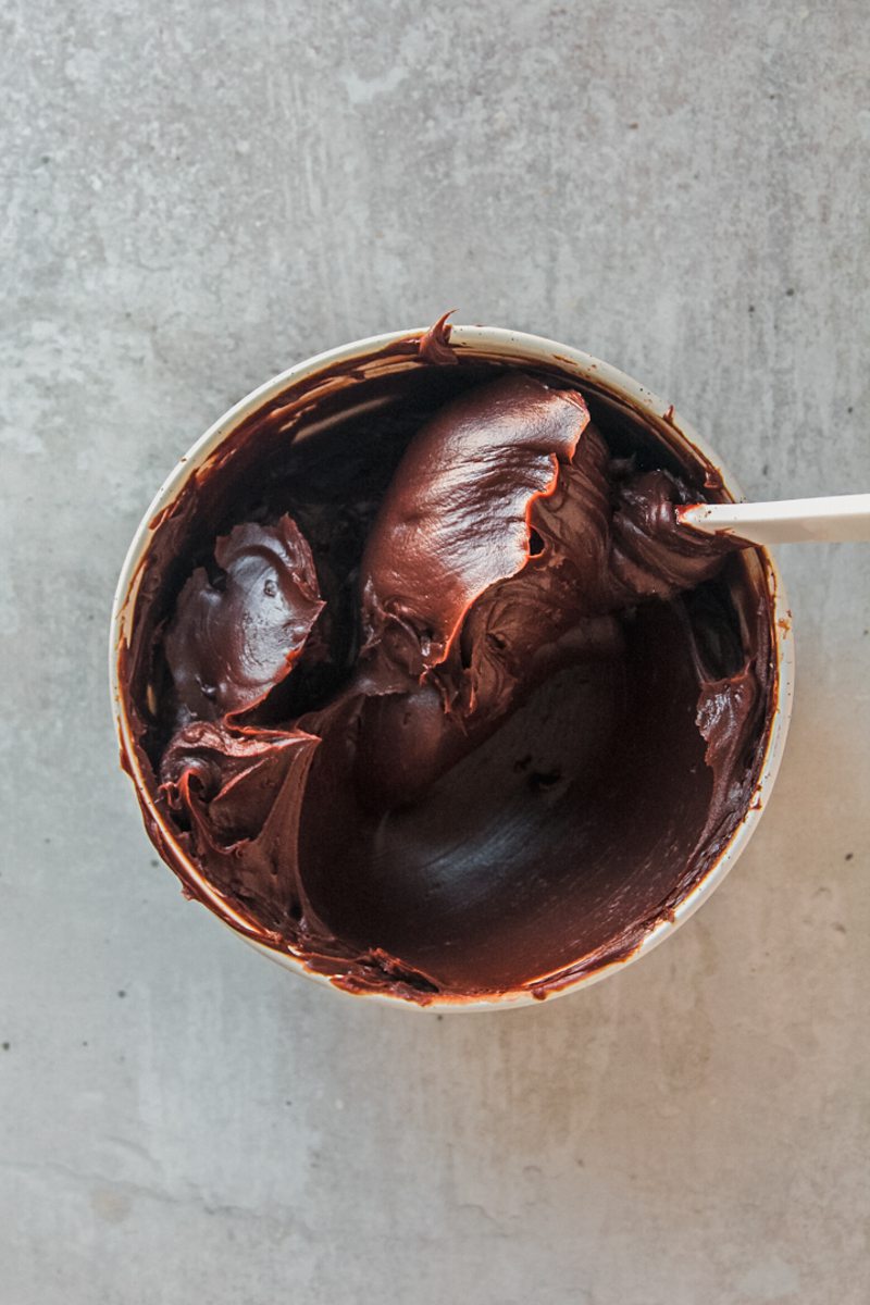 Thick chocolate ganache sits in a white ceramic bowl on a gray surface.