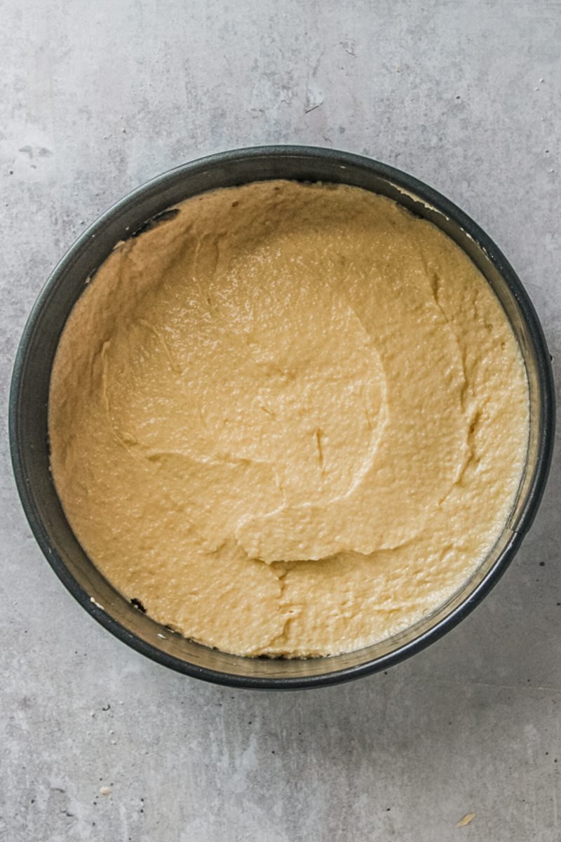 An almond cake sits in a round metal tin on a gray surface.