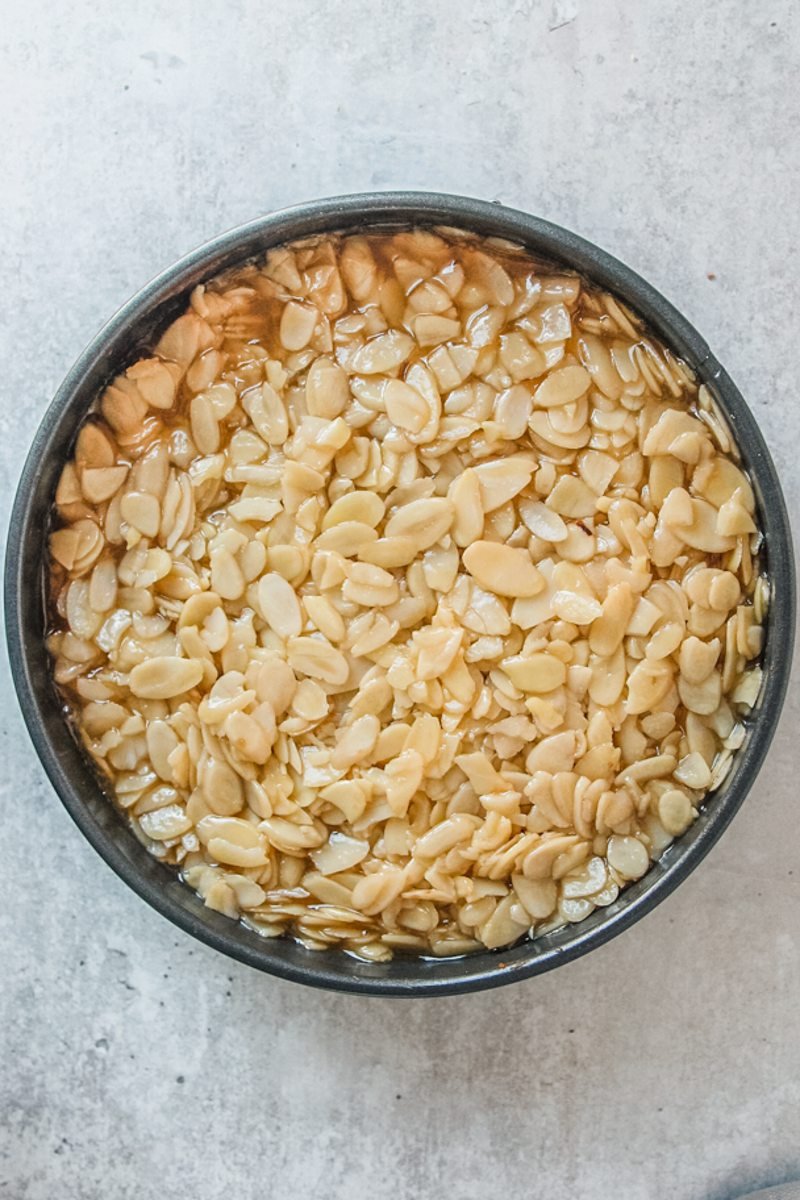 Caramelized almonds sit in a round metal cake tin on a gray surface.