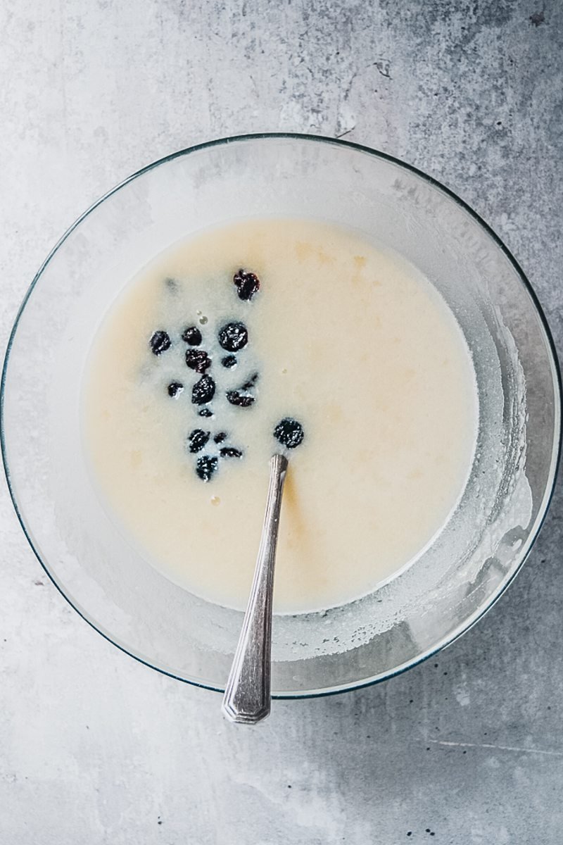 Raisins sit in a glass bowl on a gray surface.