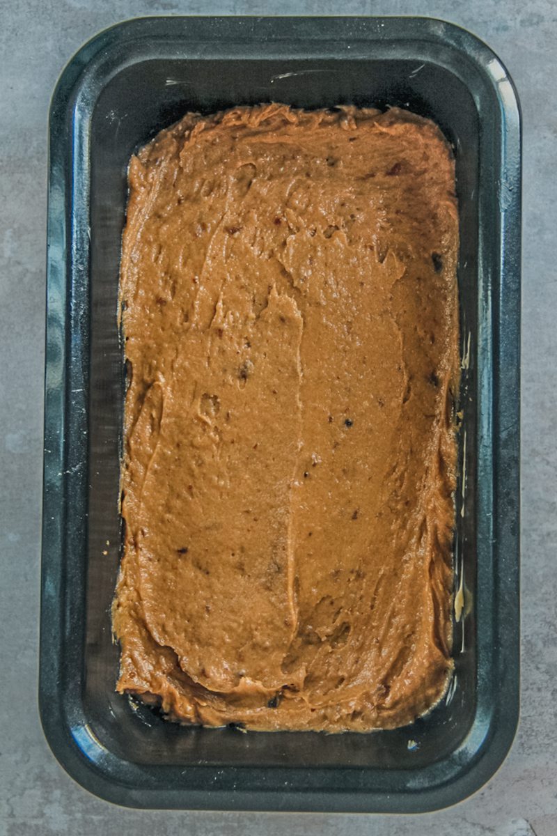 A sticky toffee pudding loaf sits in a metal tin on a gray surface.