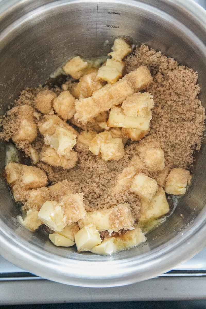 Butter and brown sugar sit in a stainless steel bowl over a cooker.