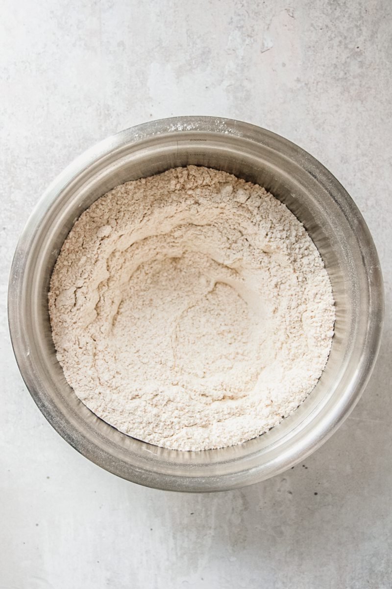 A rough breadcrumb mixture sits in a stainless steel bowl on a gray surface.