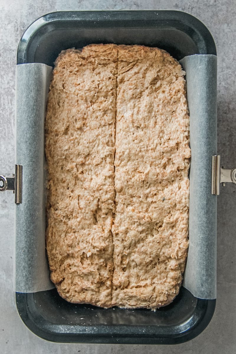 Irish brown bread dough sits in a metal loaf tin with a line cut into the center on a gray surface.