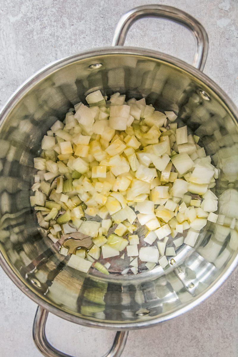 Diced onion sits in a large stainless steel pot on a gray surface.