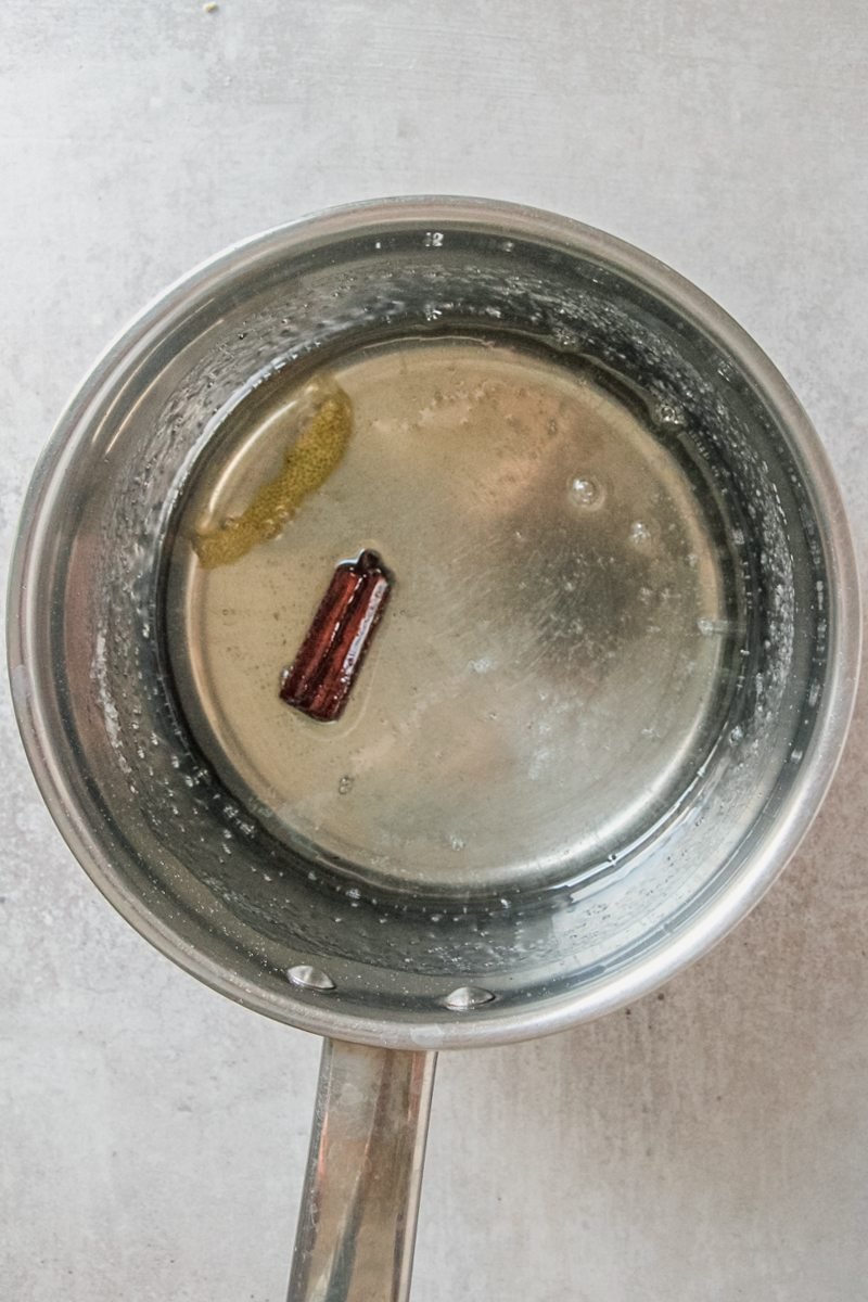 Spiced sugar syrup sits in a stainless steel saucepan on a gray surface.