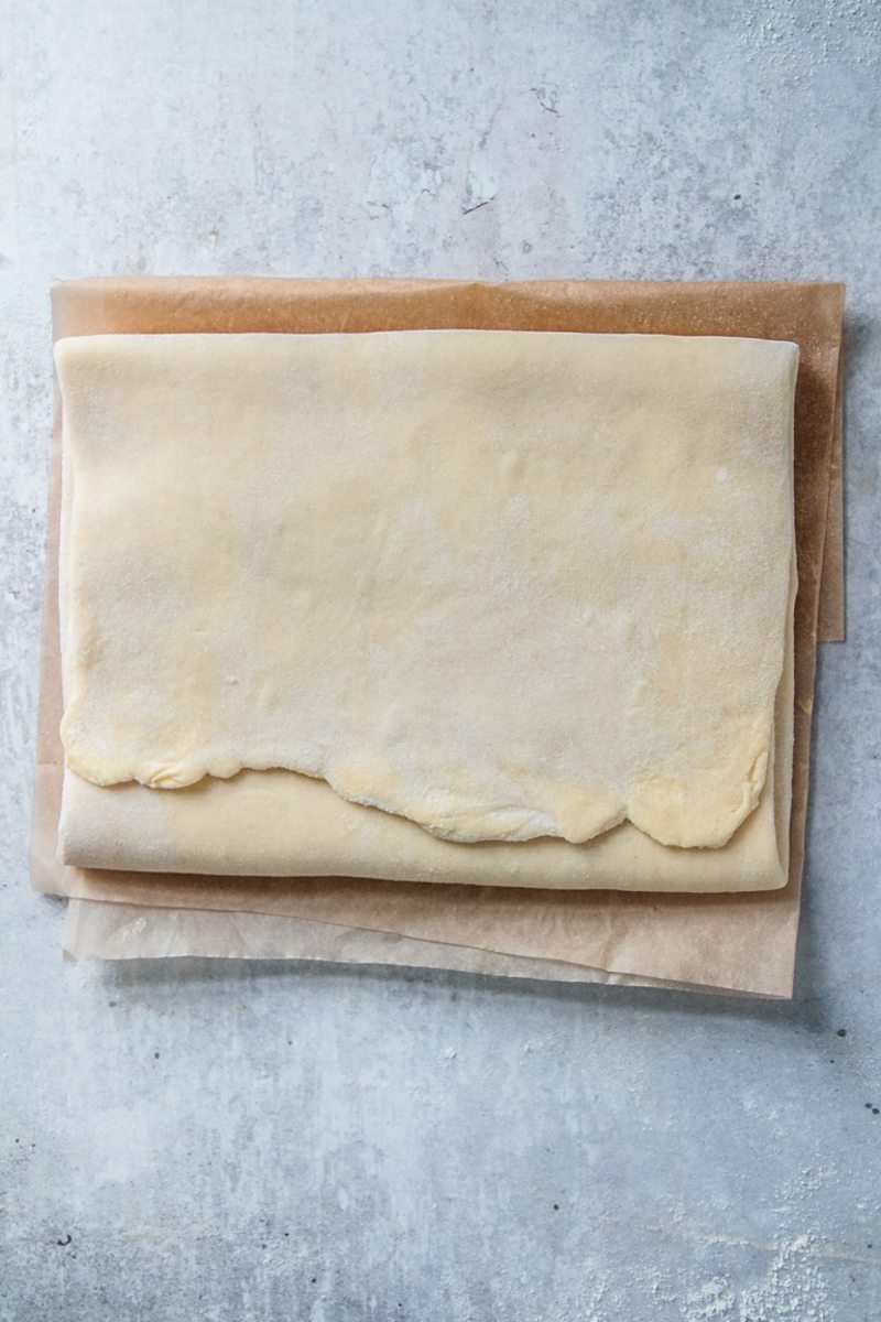 Homemade laminated dough sits on parchment paper on a gray surface.