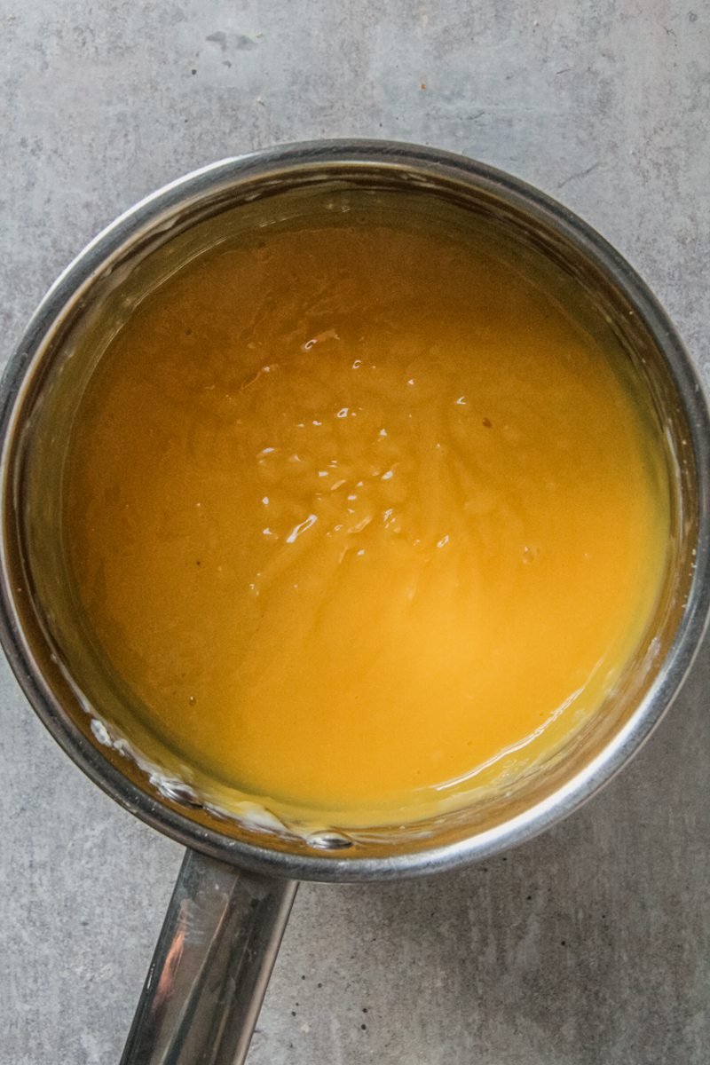 An egg yolk custard sits in a stainless steel saucepan on a gray surface.