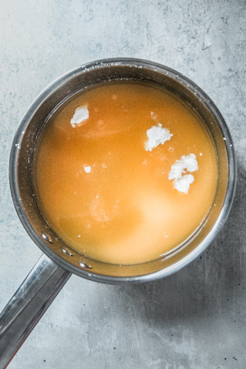 Uncooked orange pudding sits in a stainless steel saucepan on a gray surface.