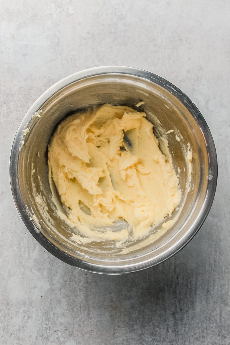 Whipped butter and sugar sit in a stainless steel bowl on a gray surface.