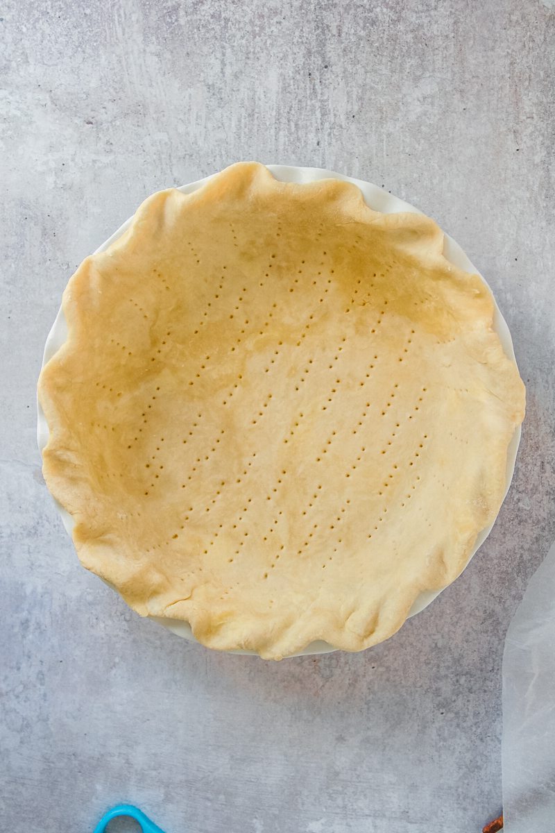 Pierced pie pastry sits pressed into a pie dish on a gray surface.