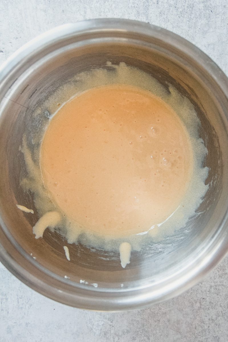 Whisked egg yolks sit in a stainless steel bowl on a gray surface.