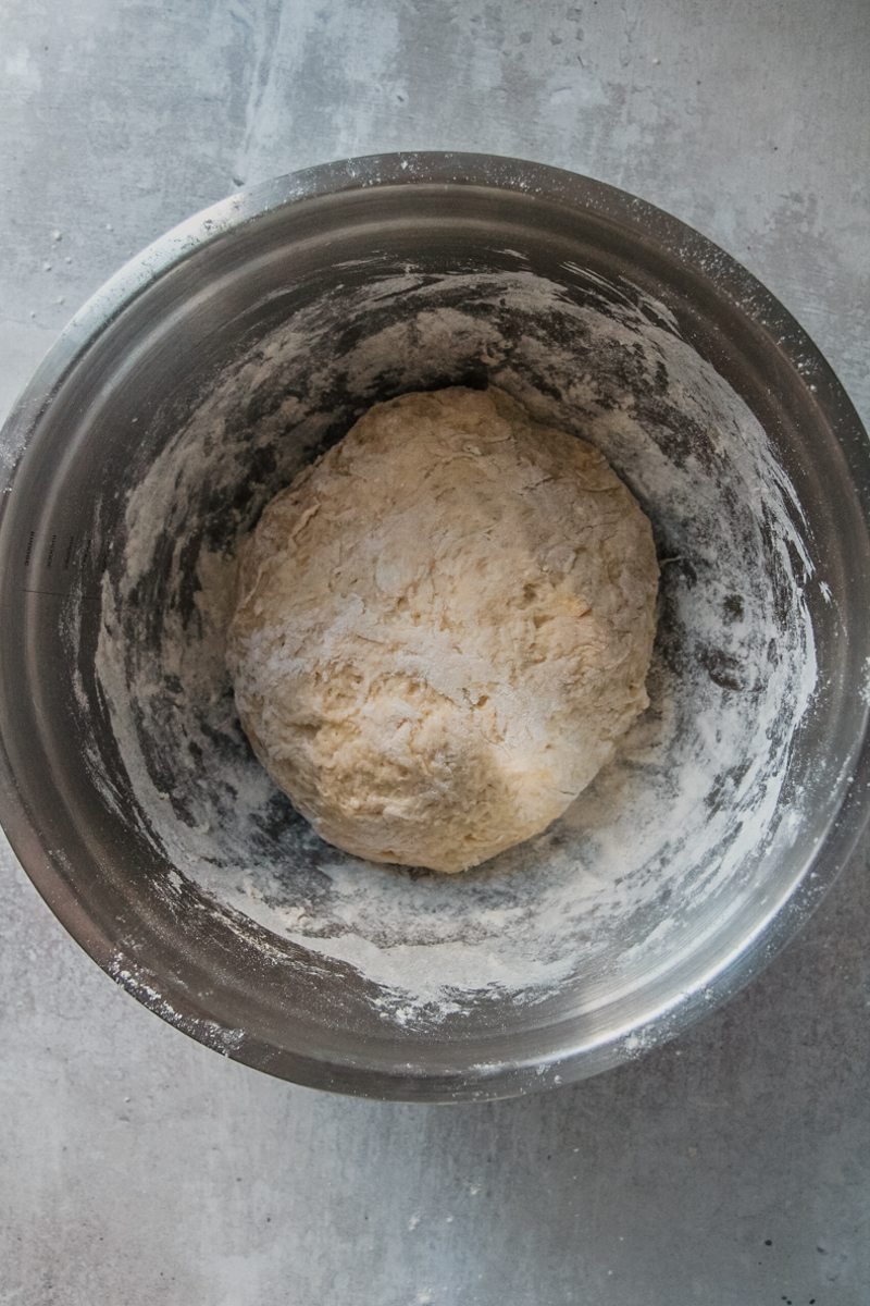 A potato bread dough sits in a stainless steel bowl on a gray surface.