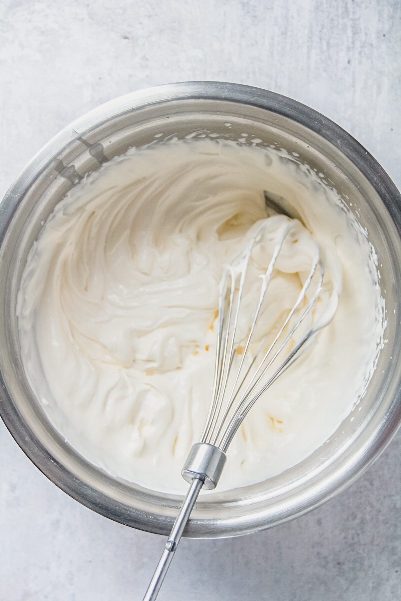 Whipped cream sits in a stainless steel bowl on a gray surface.