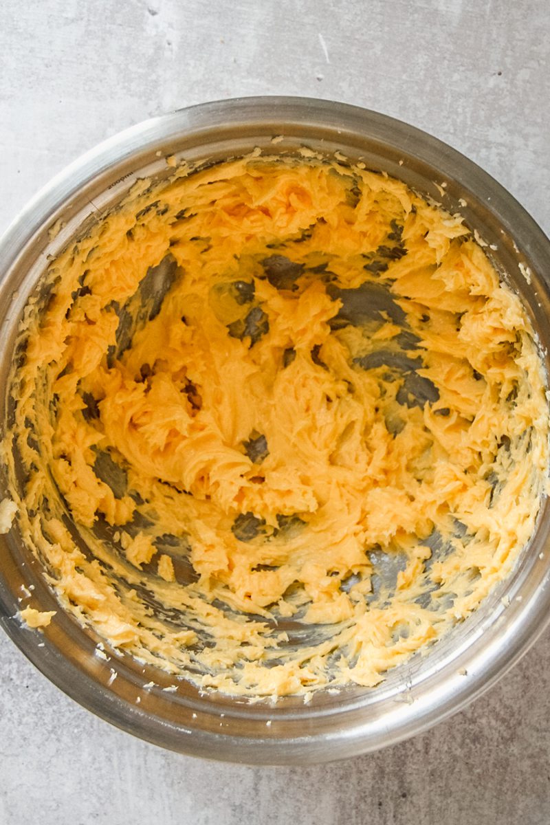 Whipped egg yolks and butter sit in a stainless steel bowl on a gray surface.