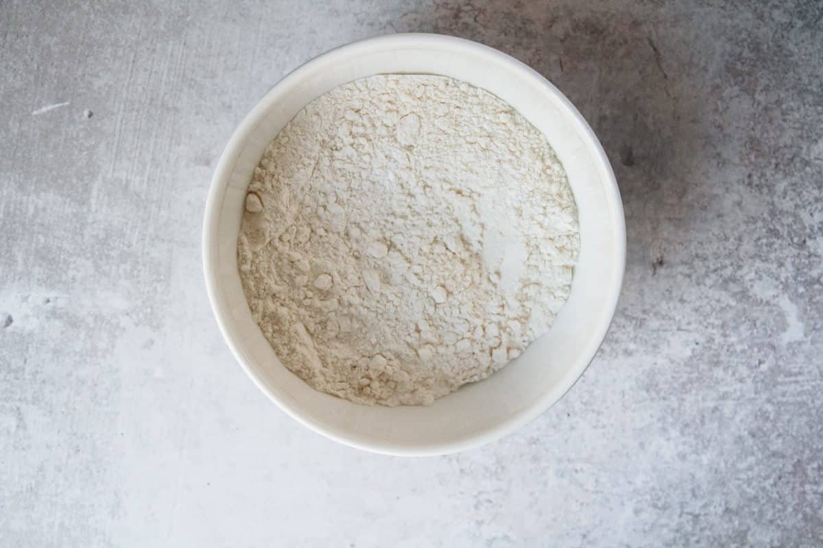 Flour and baking powder sit in a ceramic bowl on a light grey background for a Swedish Meringue Cake.