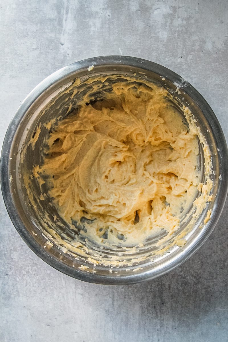 A whipped egg yolk sponge mixture sits in a stainless steel bowl on a gray surface.