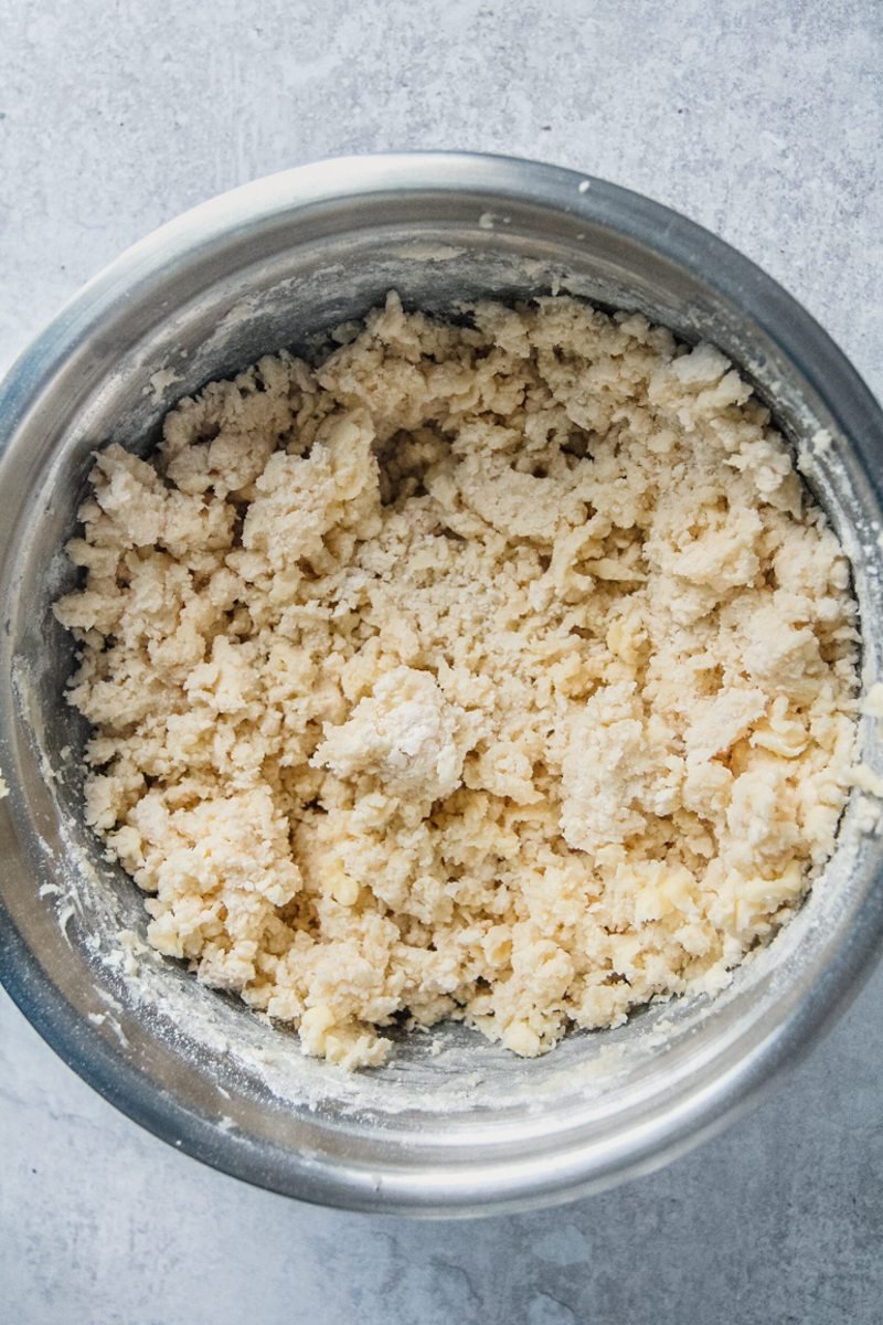 Whipped shortbread style dough sit in a stainless steel bowl on a gray surface.