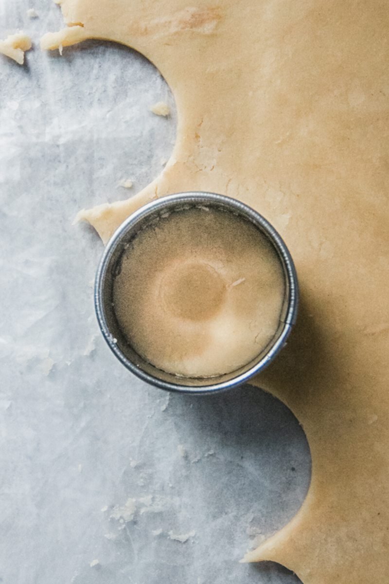 A round cookie cutter sits into a shortbread style dough that has been rolled out with an indent in the center of the cut out cookie dough.