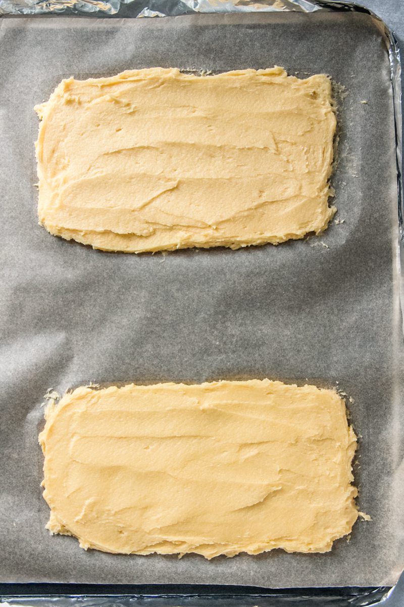 Two rectangle egg yolk sponge mixtures sit on a lined baking tray.