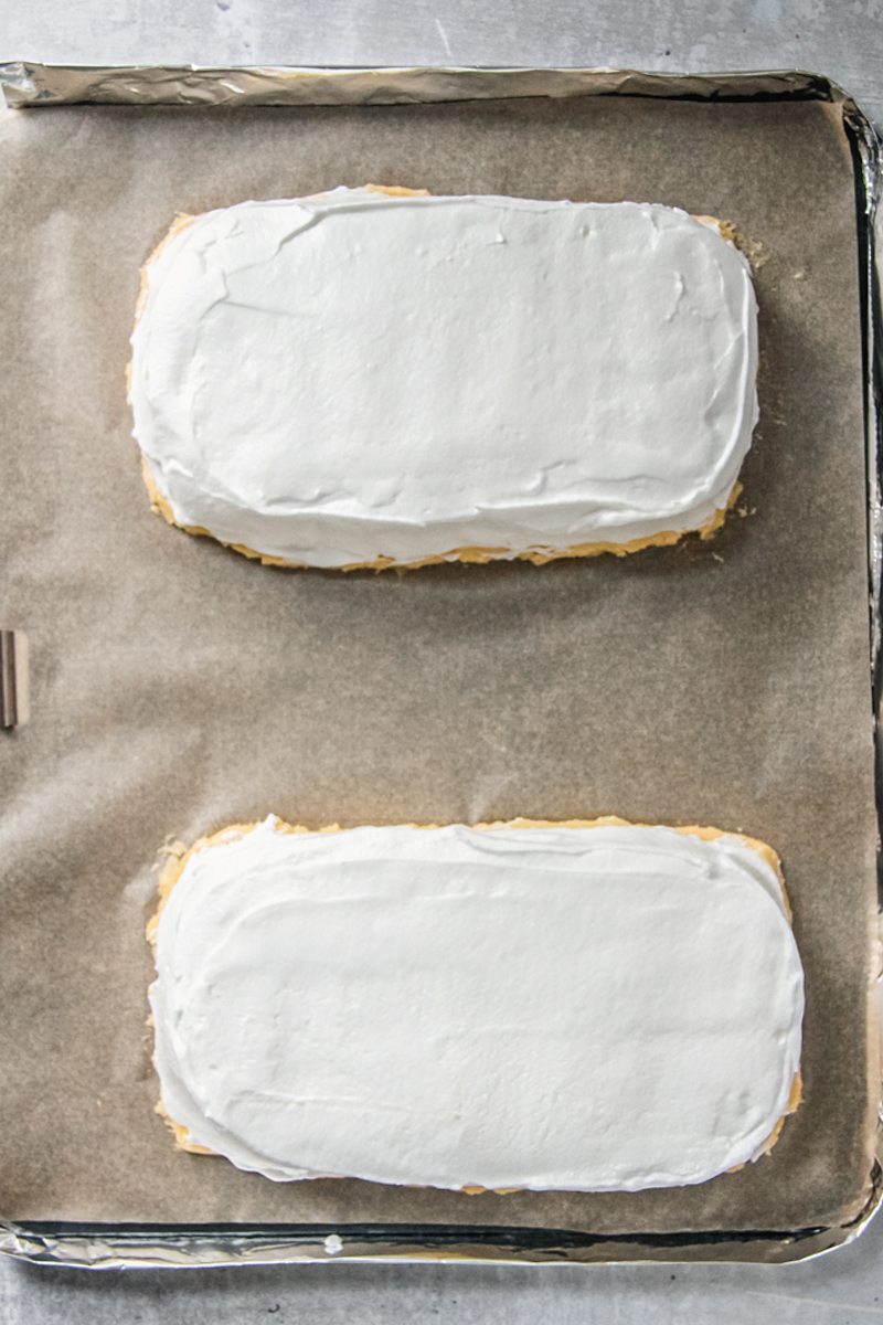 Shaped meringue rectangles sit on top of egg yolk sponge sit on a lined baking tray.