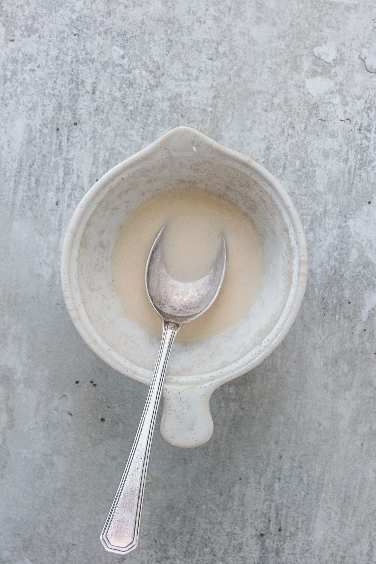 A slurry of milk and flour sits in a small ceramic pouring bowl on a gray surface.
