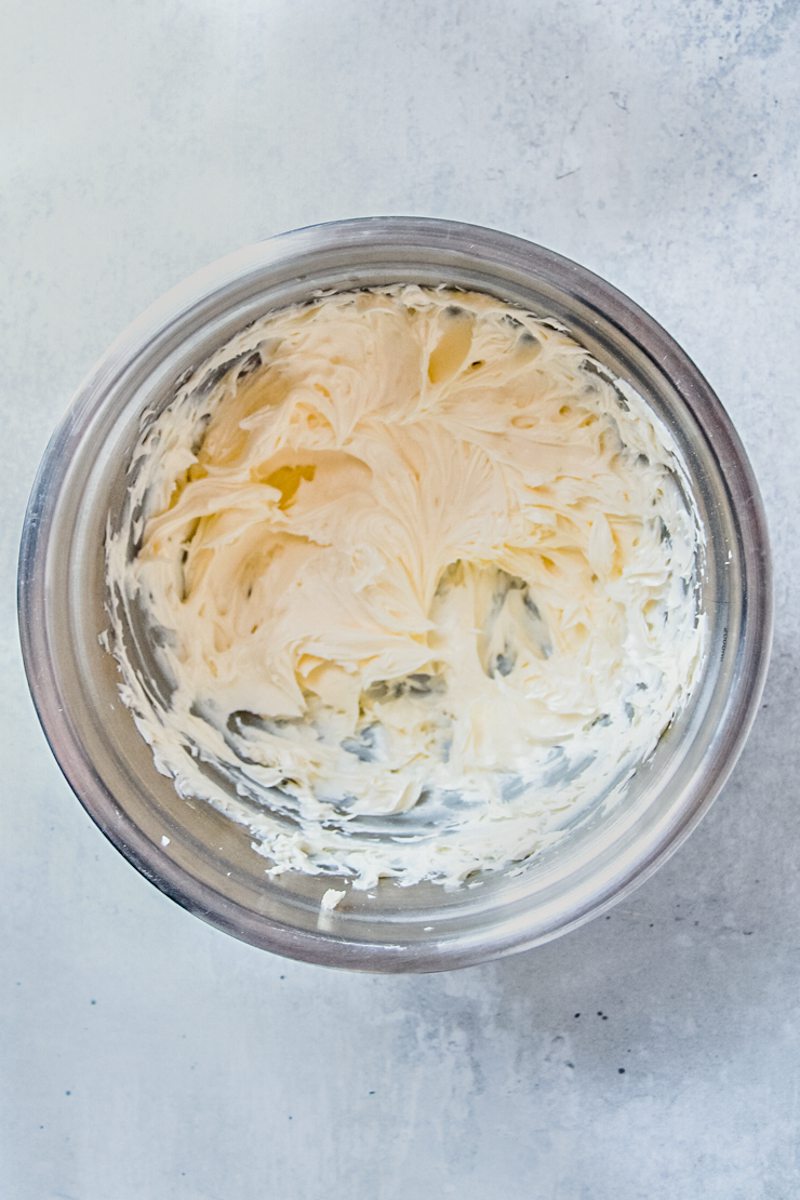 Whipped butter and powdered sugar sit in a stainless steel bowl on a gray surface.