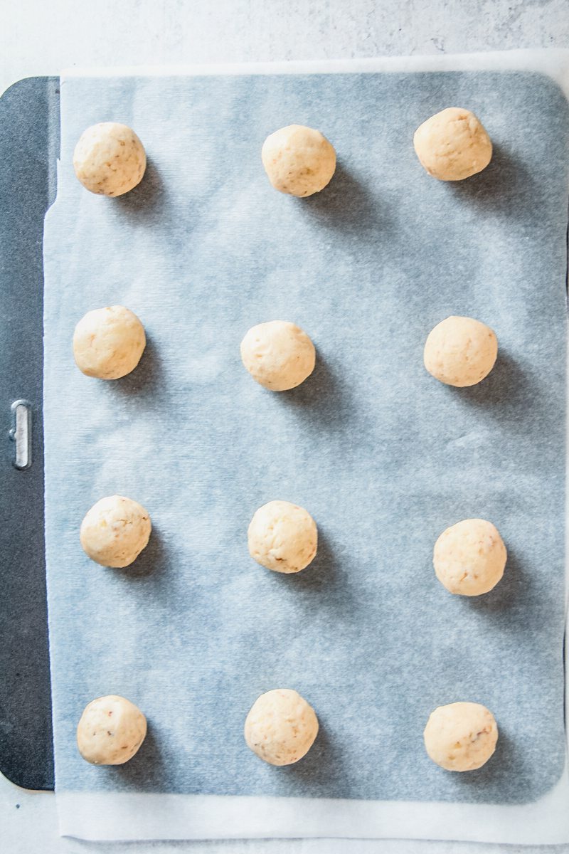 Unbaked Polvorones or Mexican Wedding Cookie balls sit on a lined baking tray on a gray surface.