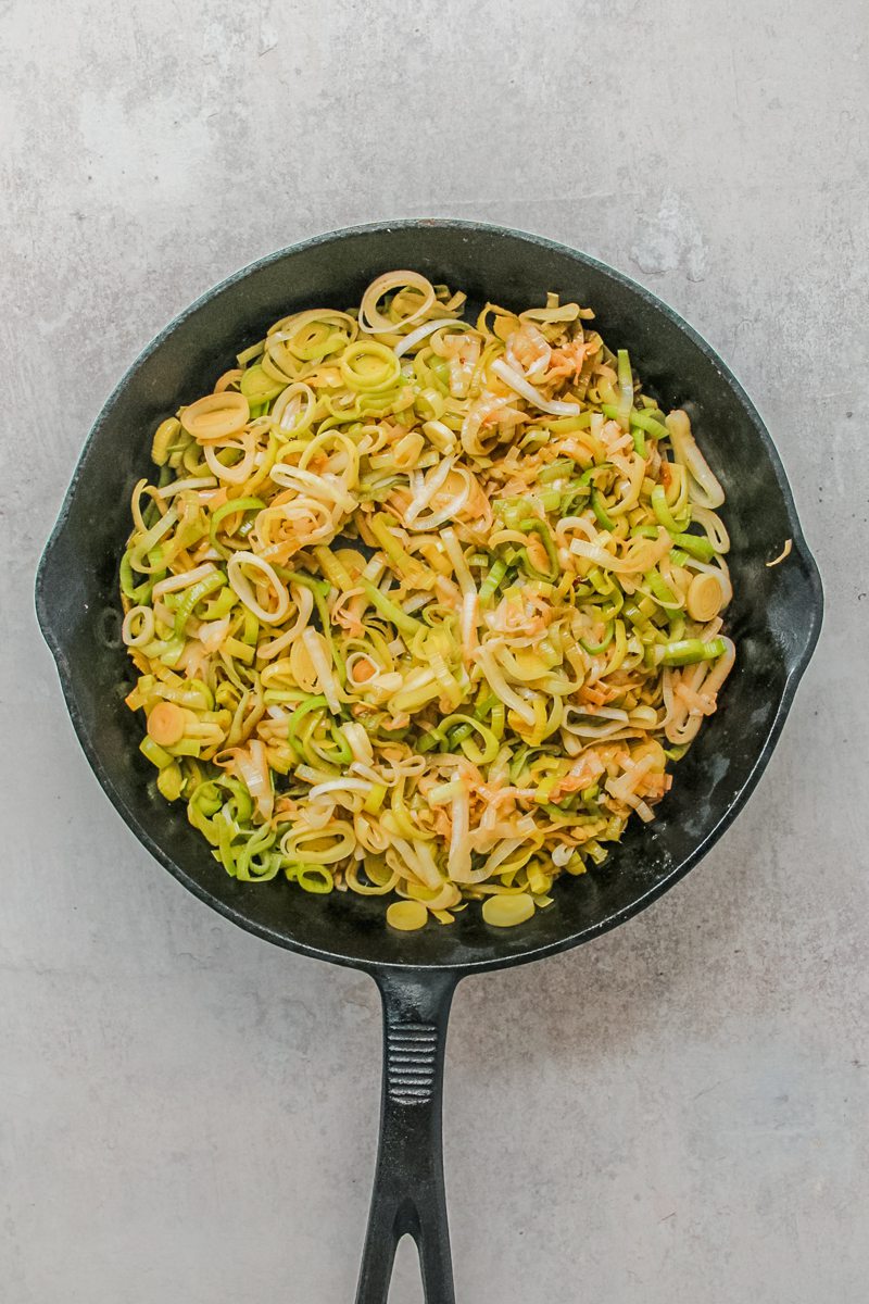 Finely sliced leeks sit on a cast iron skillet on a gray surface.