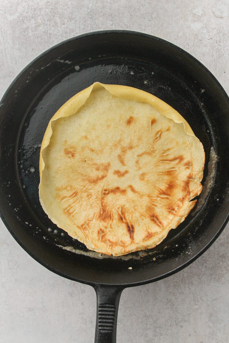 A German pancake cooks in a cast iron skillet on a gray surface.