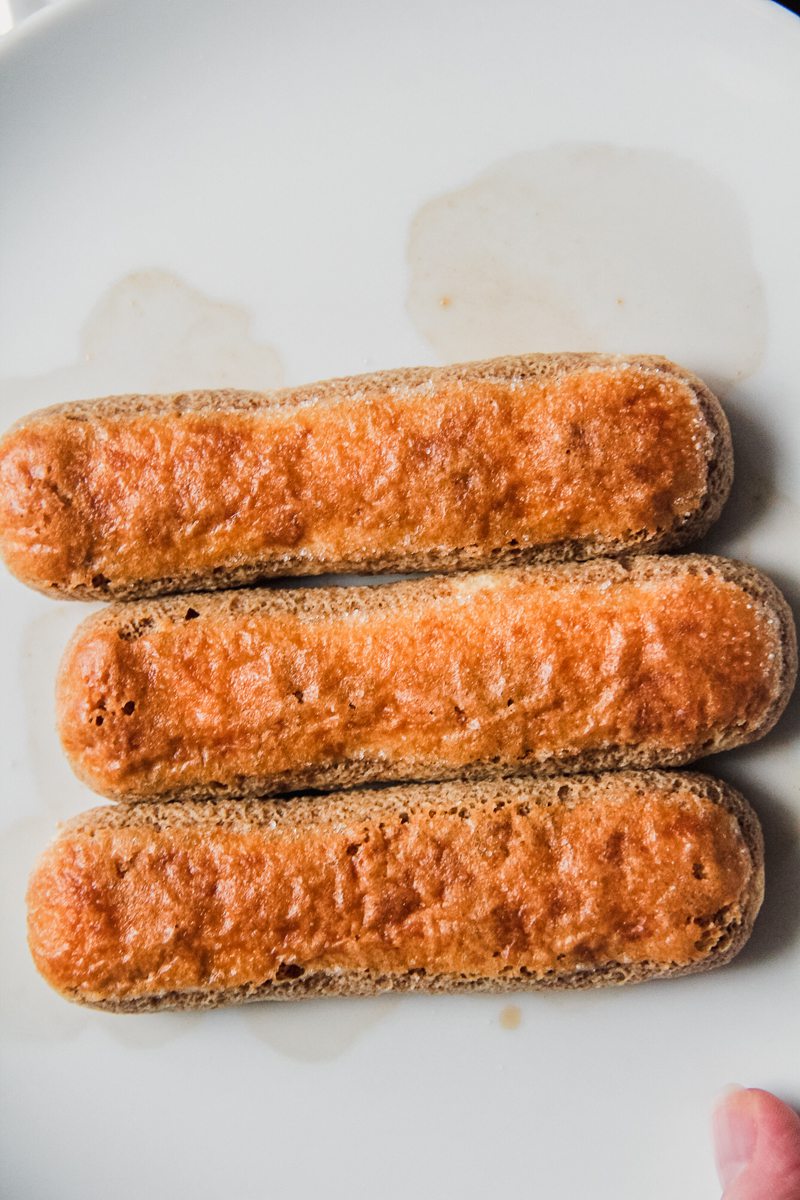 Sponge fingers soaking up coffee sit in a white ceramic plate.