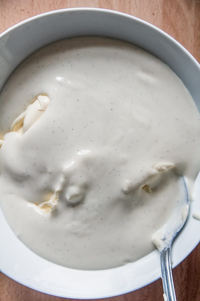 A custard and mascarpone mixture sits in a white ceramic bowl on a wooden surface.