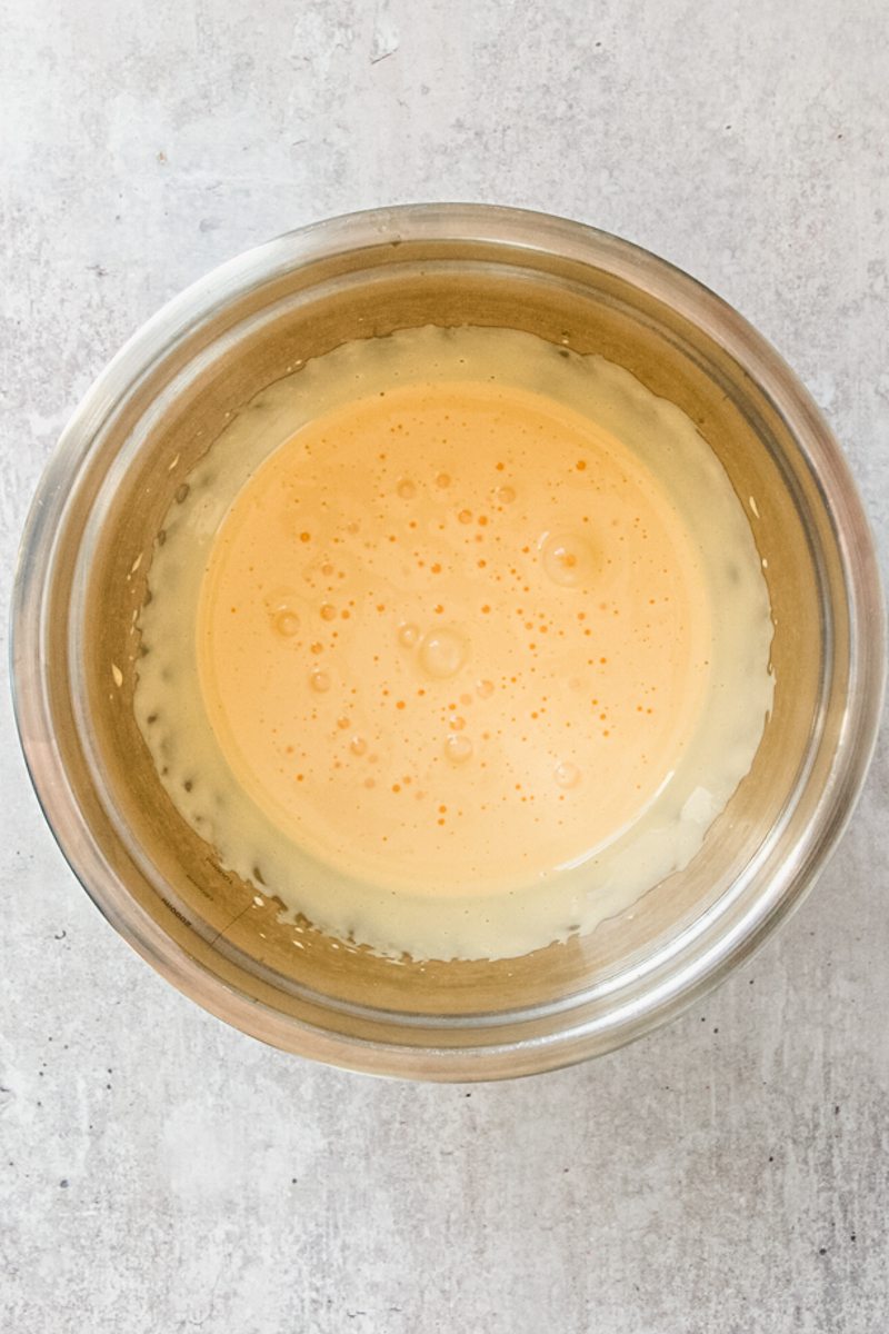 Whipped egg yolks sit in a stainless steel bowl on a gray surface.