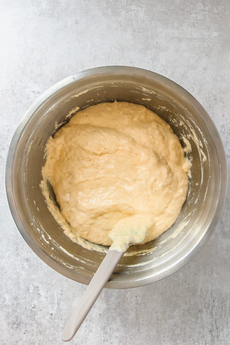 Tres Leches cake batter sits in a stainless steel bowl on a gray surface.