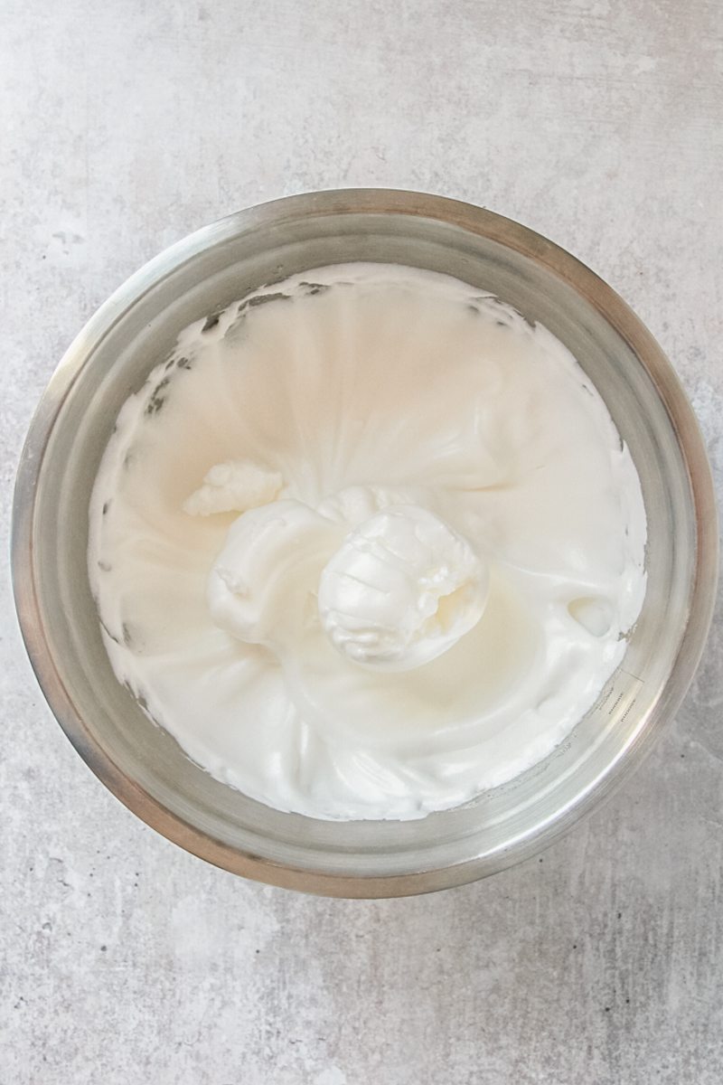 Whipped egg whites sit in a stainless steel bowl on a gray surface.