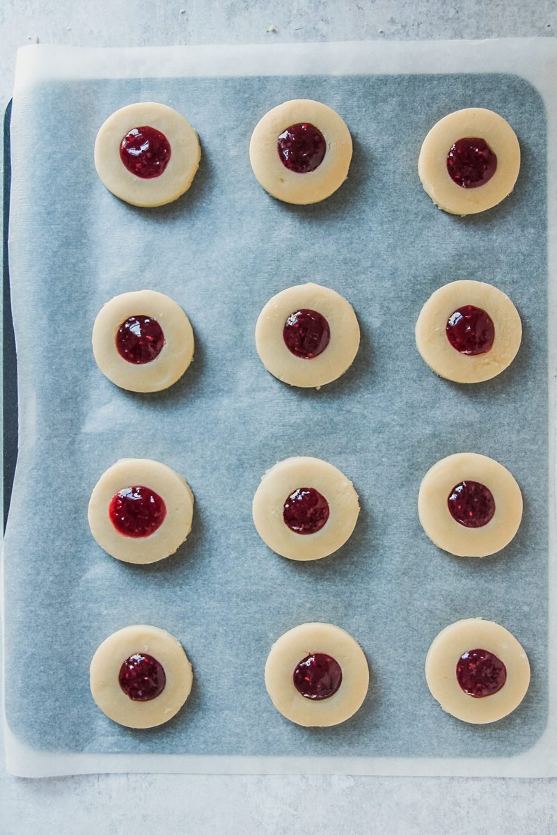 Shortbread style round cookies sit on a parchment paper lined baking tray on a gray surface.