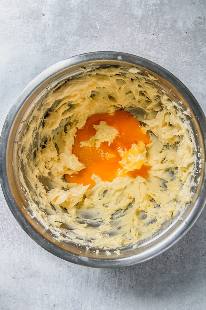 An egg yolk sits in whipped butter in a stainless steel bowl on a gray surface.